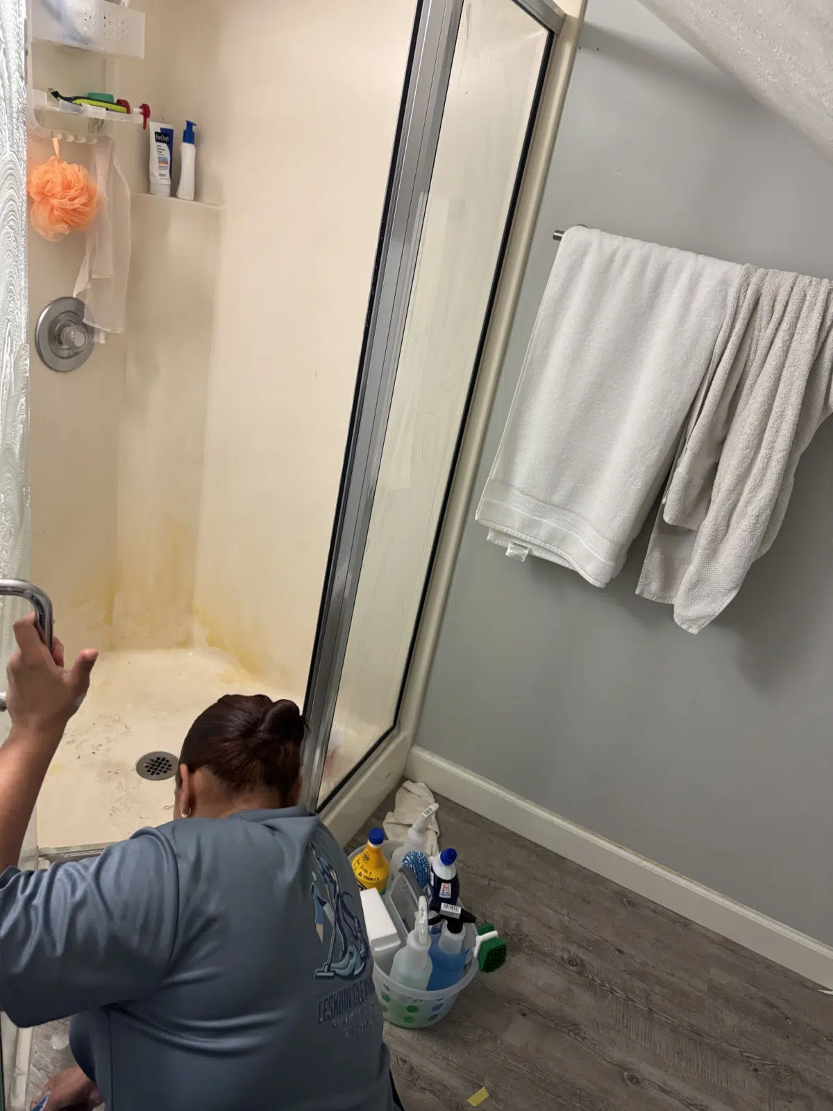 Cleaner scrubbing a stained shower stall with supplies nearby — Leskuin Cleaning LLC in Springfield